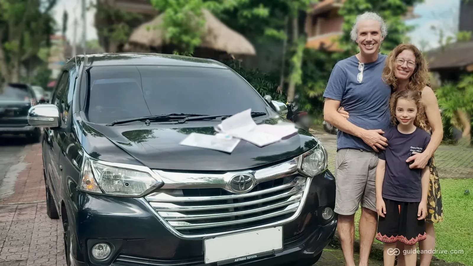 A family beside their black Toyota Avanza rental, the rental papers on the bonnet