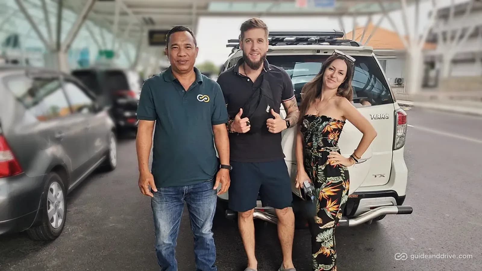 Guide and Drive driver in a branded polo with two guests beside their car